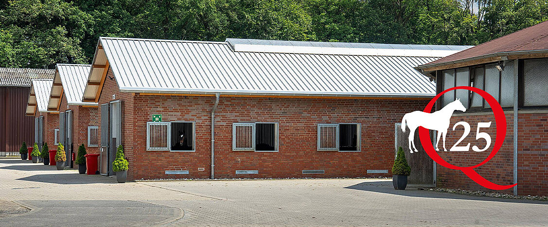 Außenansicht moderner Pferdestallungen aus rotem Backstein mit weißen Metalldächern, mehreren Stallfenstern und gepflastertem Hof; rechts ein aufgesetztes Logo mit weißem Pferd und roter „Q25“-Kennzeichnung.