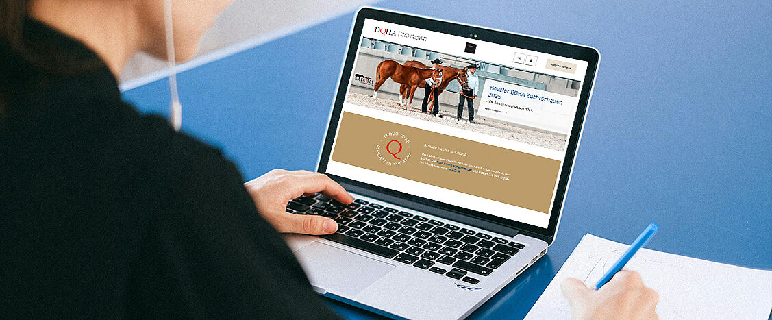 Person arbeitet am Laptop und betrachtet die DQHA-Webseite mit Informationen zu einer Zuchtschau; daneben liegen Notizen und ein Stift.